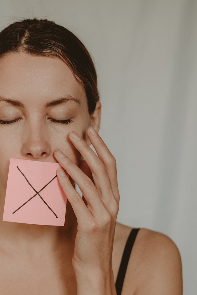 A woman with a sticky note with an “X” drawn on it.