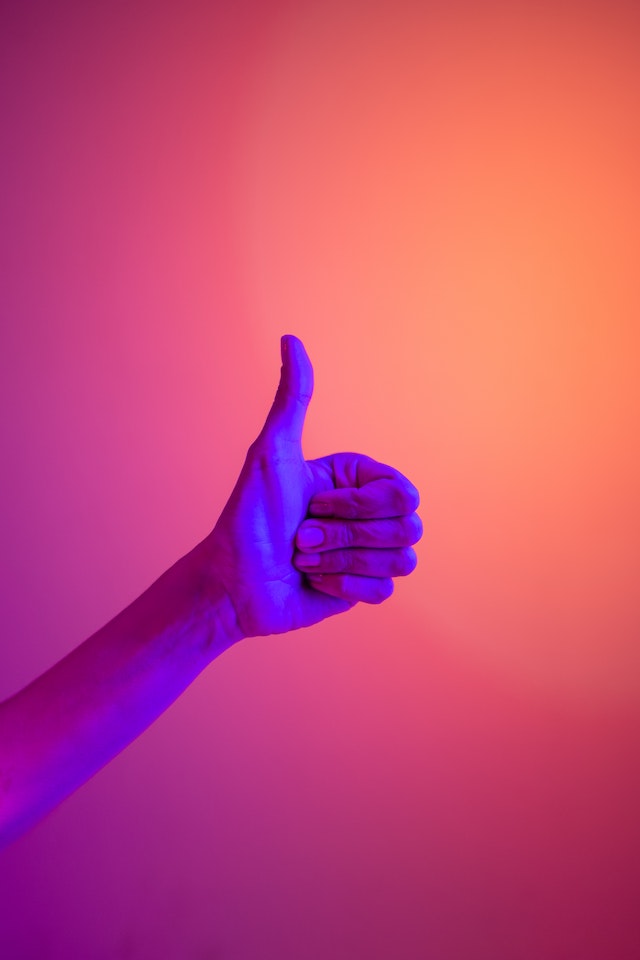 A hand throwing up a thumbs-up sign against a multi-color background.