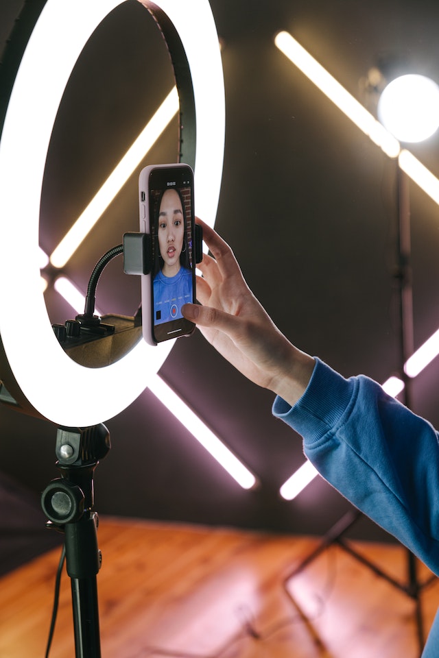 A woman holds her camera to the ring light, ready to make monetized content.