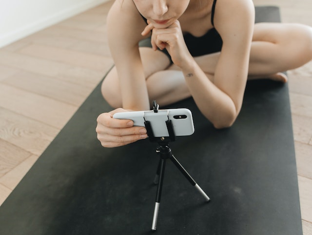 A woman sets up her phone on a tripod to begin recording her yoga routine.