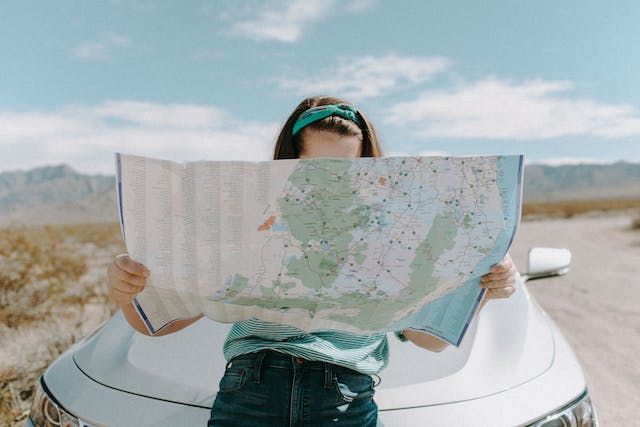 A travel influencer sits on the hood of her car and looks at a map.