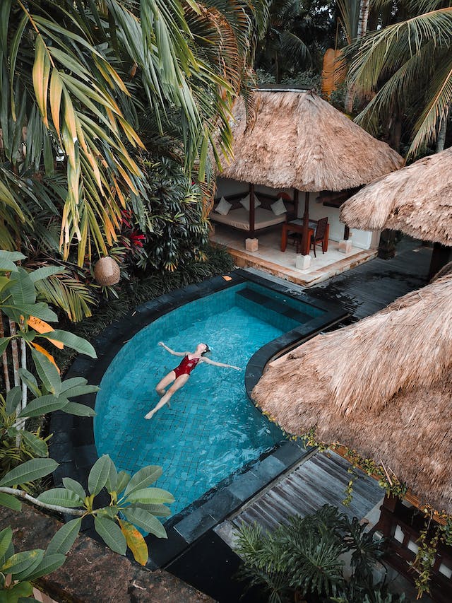 An aerial view of an IG travel content creator floating in her tropical luxury hotel pool.