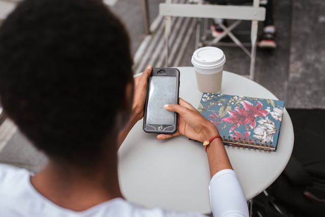 Une femme utilise son téléphone portable et a un carnet de notes et une tasse de café sur la table.