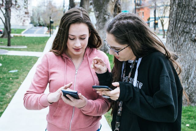 Due donne scorrono i loro cellulari mentre si trovano in un parco.