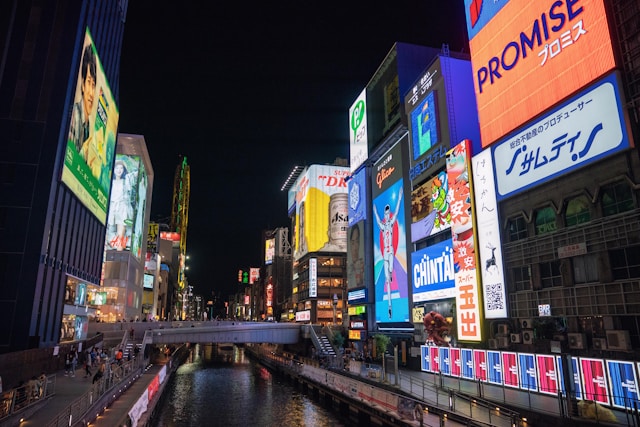 A canal street with many neon billboard ads illuminating at night.