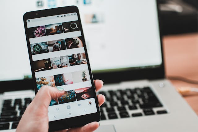 A person holding a phone and looking at a gallery in front of a laptop.