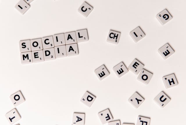 "소셜 미디어"라는 단어를 형성하는 스크래블 타일과 흰색 표면에 흩어져 있는 몇 개의 타일.