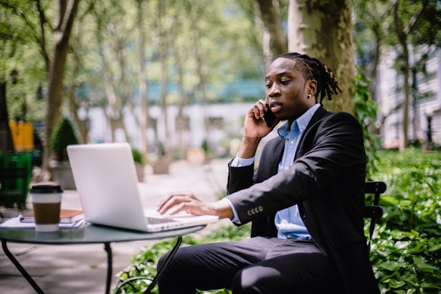 Un homme en costume d'affaires utilise son téléphone et son ordinateur portable à l'extérieur.