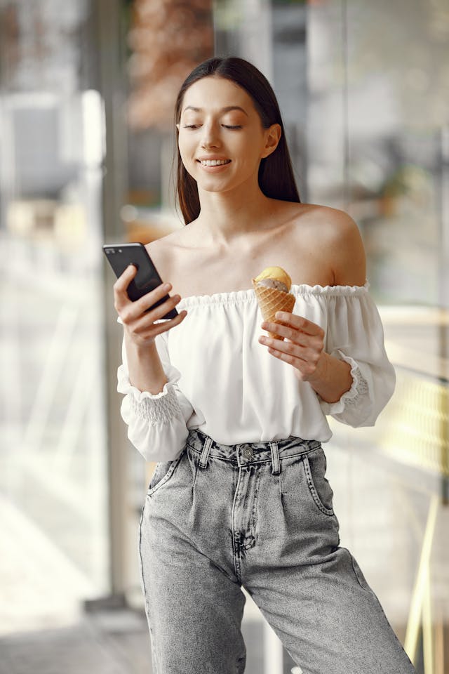 A woman looks at her phone while eating ice cream.